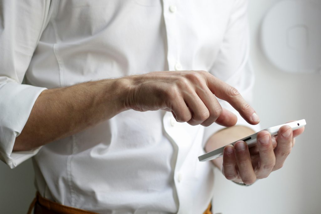 Homme en chemise blanche utilisant un smartphone pour contacter un service de création d’entreprise.